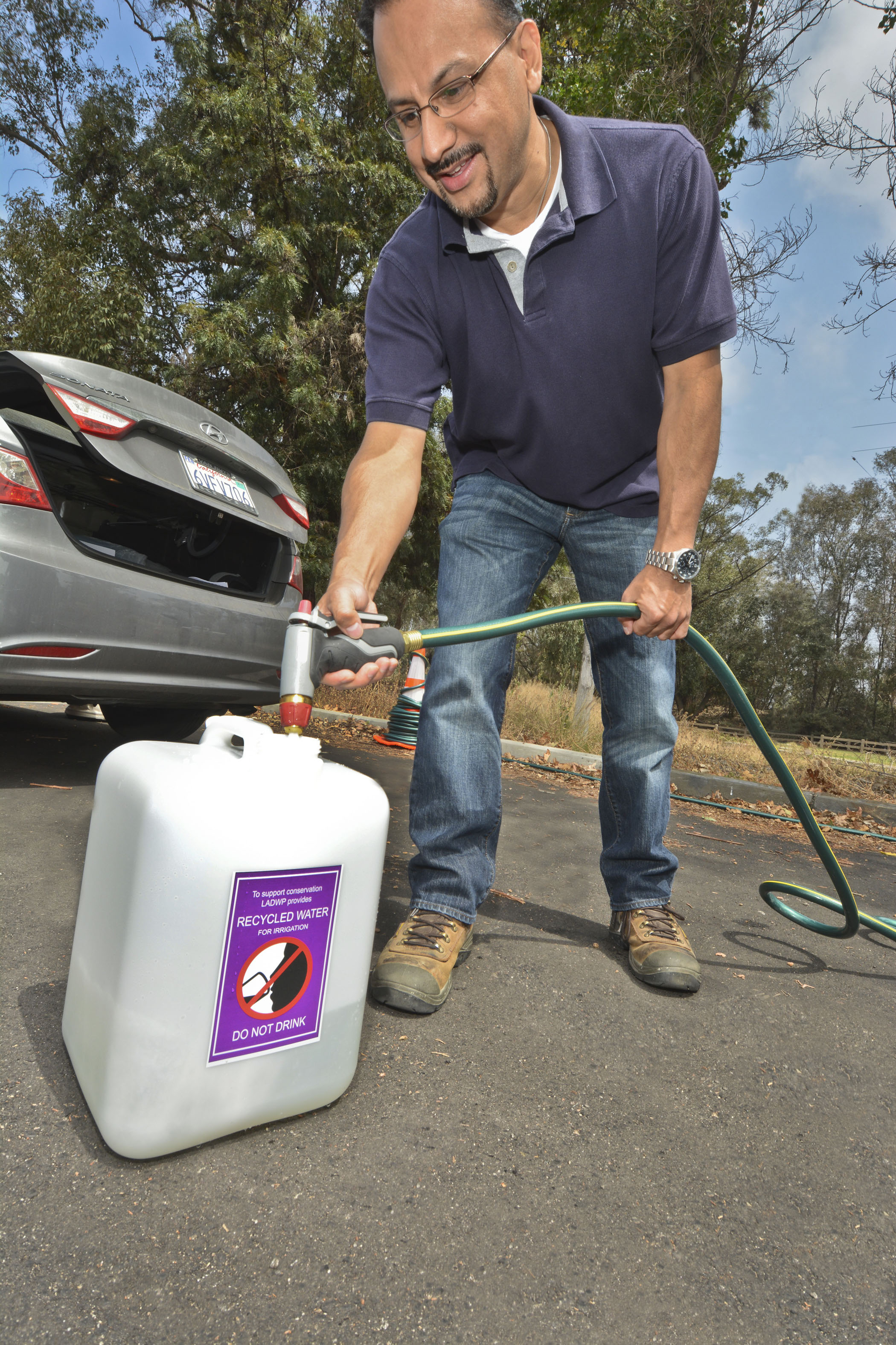 Man pouring recycled water into a labeled tight lid container at a recycled water fill station.