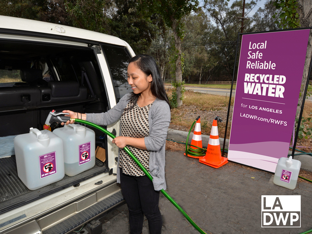 Woman pouring recycled water into a labeled tight lid container at a recycled water fill station.
