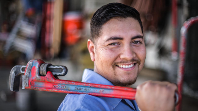 Man holding a wrench in right hand laying on right shoulder smiling. 