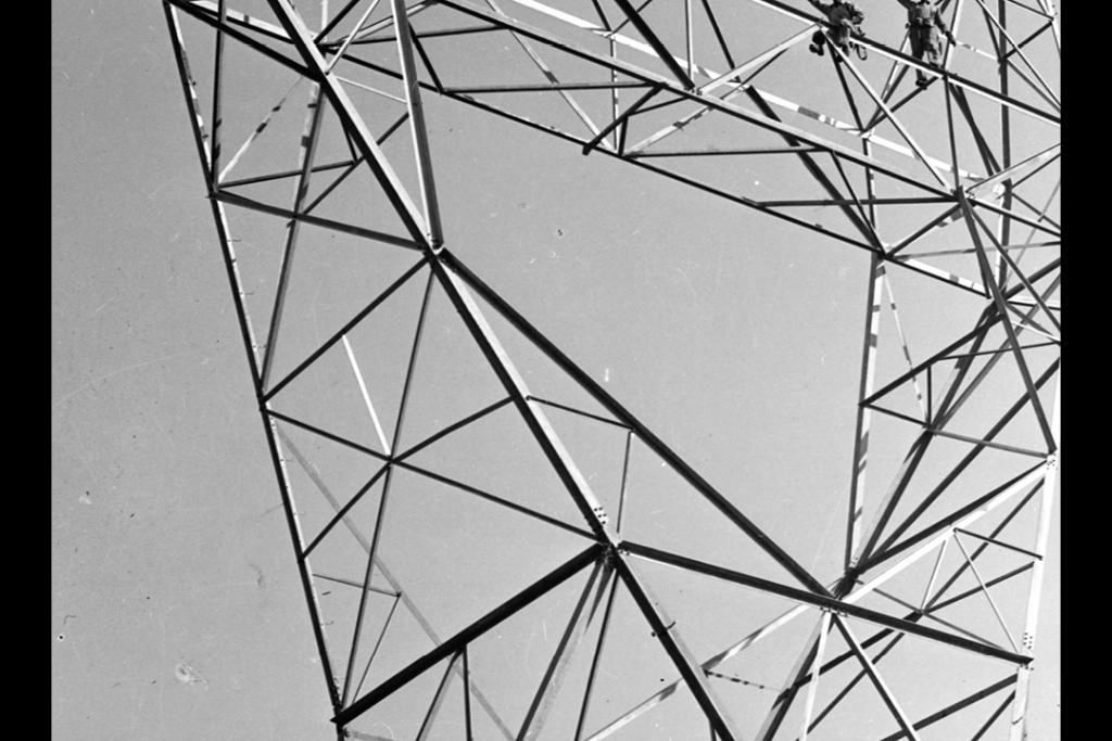 Upward view of workers atop power transmission tower
