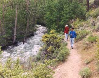 Pair of people walking along a trail next to flowing river