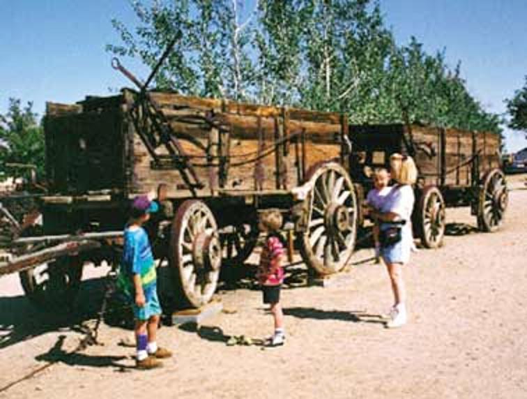 Four museum patrons standing next to and looking at a wooden stage wagon