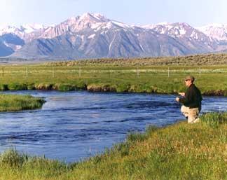 Man fishing at rivers edge, snow capped mountains in background