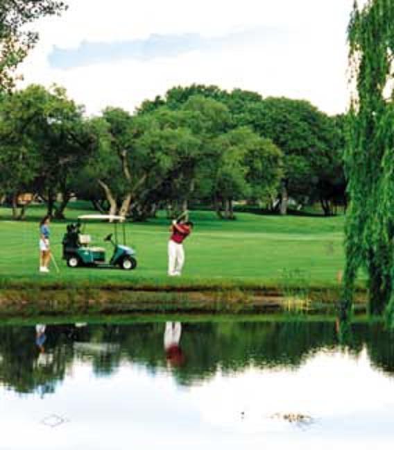 Image of Golf course, Golfer standing next to golf cart, and another golfer preparing for a swing, water edge in foreground