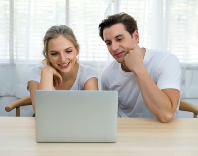 Smiling lady and man are sitting down looking at a laptop screen. 