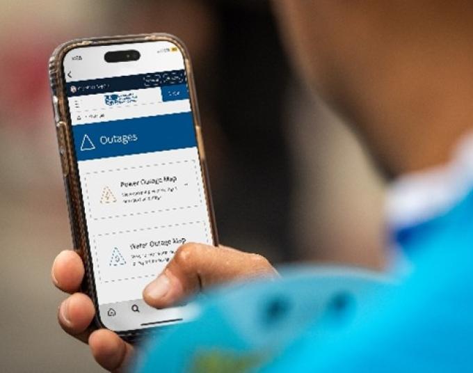Person holding cell phone. The phone’s screen is showing information about power outages.